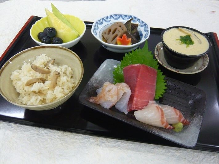刺身の盛り合わせに茶碗蒸し、炊き込みご飯、メロンとぶどう、煮物などが並べられている。