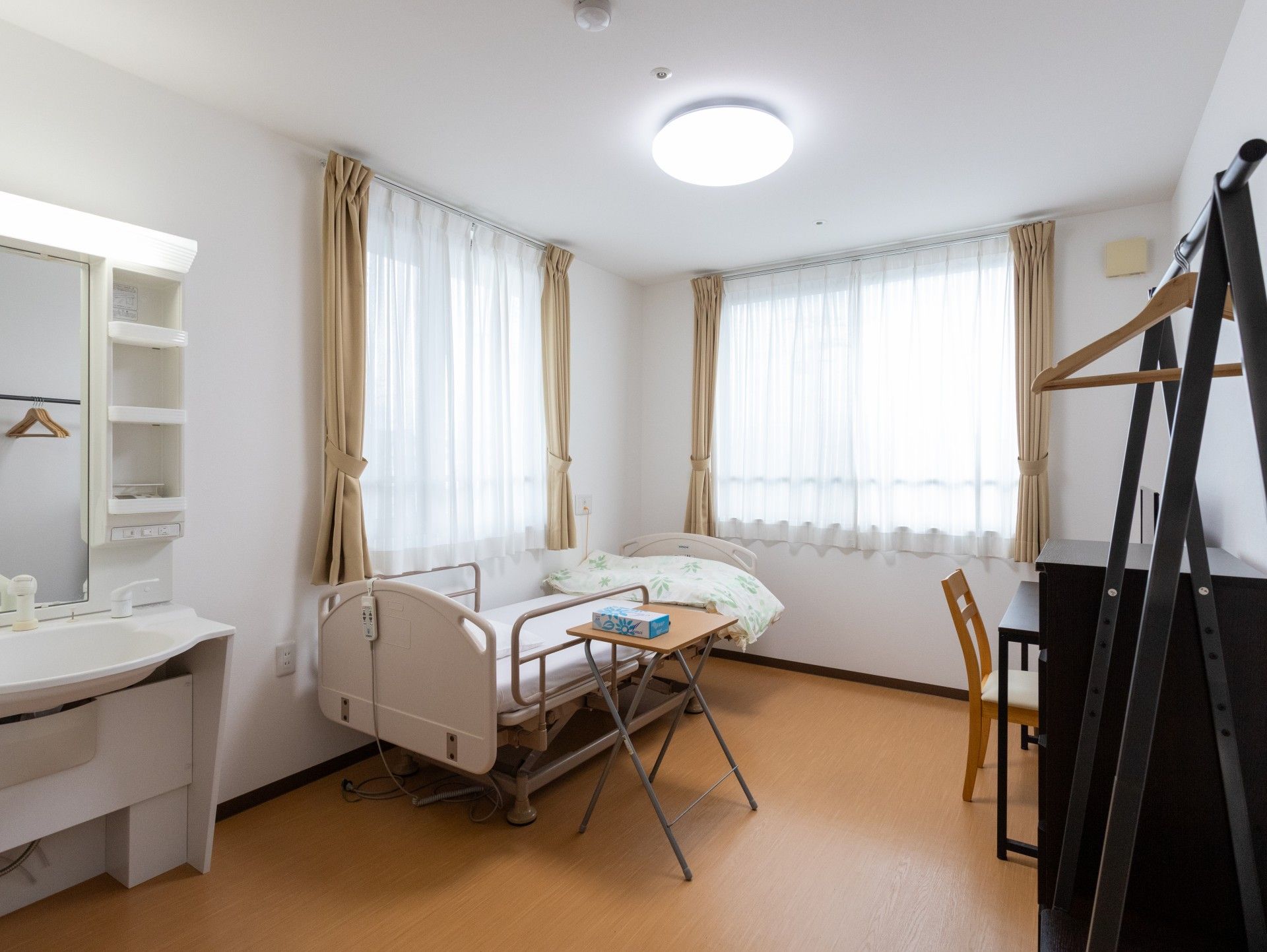 フローリングの部屋には車いす対応の洗面所やゴミ箱、カーテンが付いた窓がある。