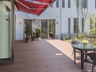 赤い屋根が付いたウッドデッキが敷かれたテラスには花が飾られたガーデン用テーブルセットもある。