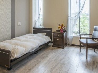 寝具付きのベッドやミニタンスが置かれたフローリングの部屋には花も飾られ、緊急通報装置もある。