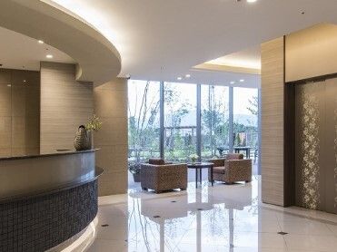 エレベーターが設置され、その前にはフロントがあり、奥の窓のそばには応接セットが置かれている。