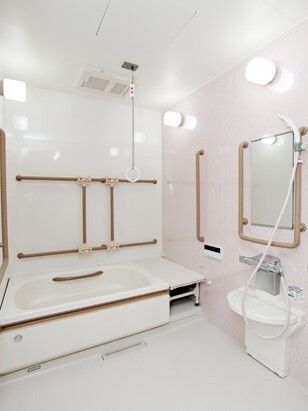 白を基調とした一人用の浴槽が設置された浴室には、ブラウン系の手すりがたくさんあり、浴槽横にはベンチもある。