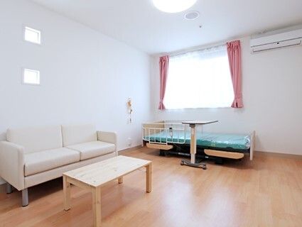 レースカーテンとカーテンが付いたおおきな窓があるフローリングの部屋。ベッドやソファ、ローテーブルがある。