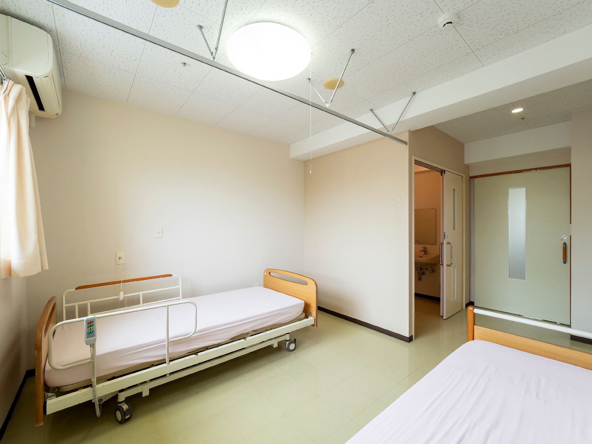 隣同士に座り、高齢女性の赤いロープを使ったエクササイズをサポートしているブルーのユニフォームを着た男性スタッフ。
