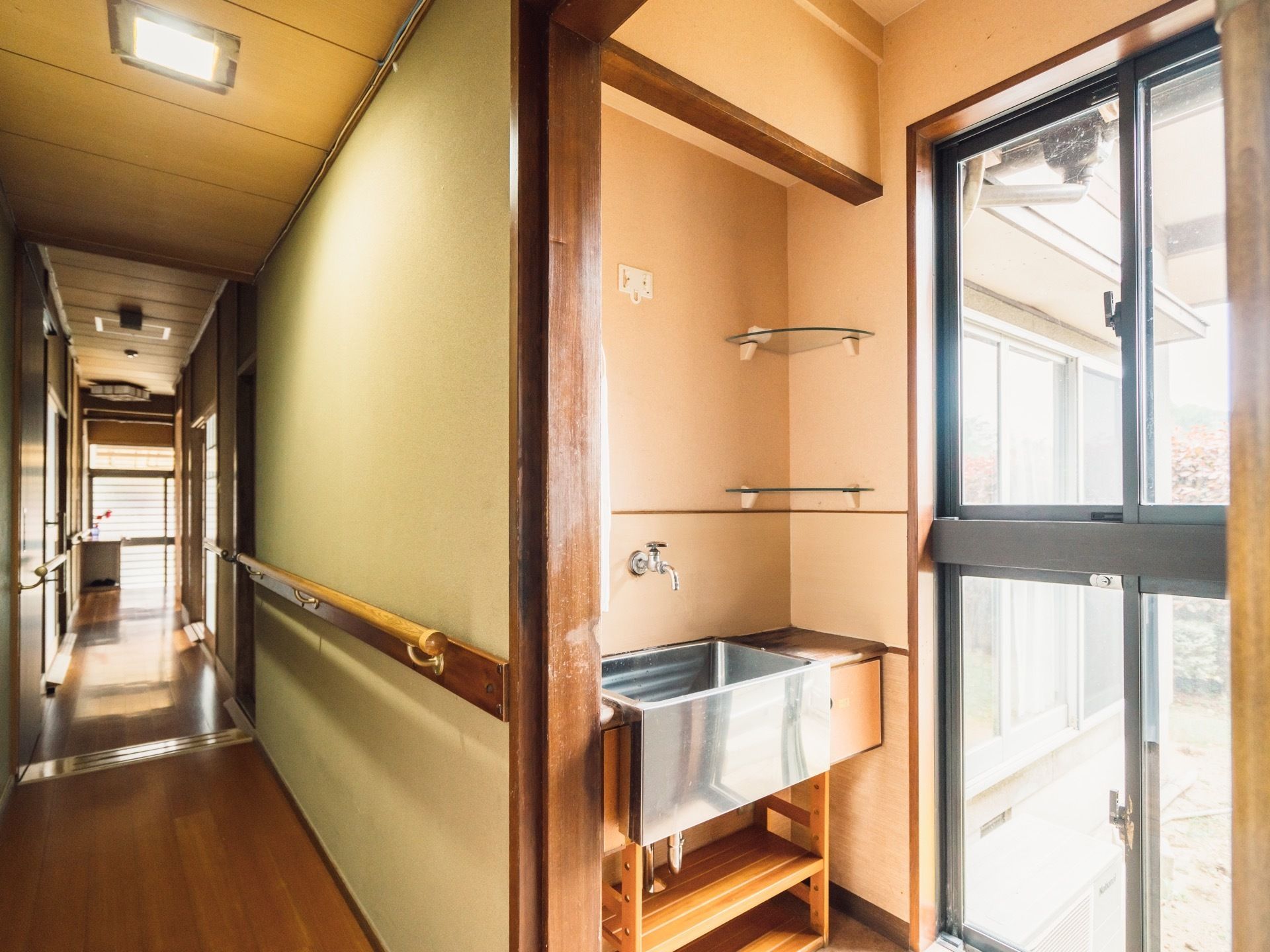 落ち着いた和風建築の室内にある長い廊下。壁には手すりが設置されている。窓の側にはステンレス製の洗面台がある。