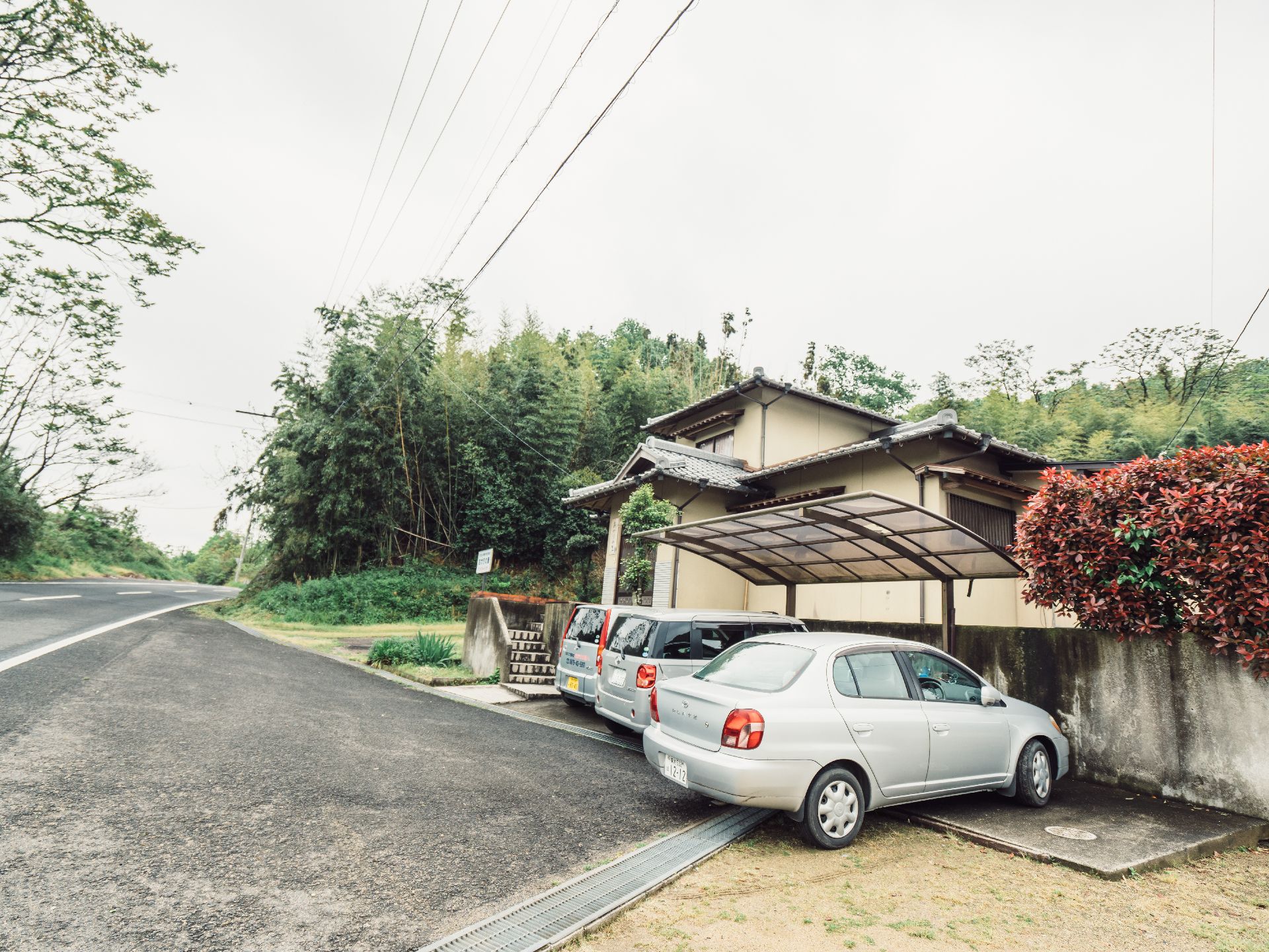 2階建ての瓦屋根の付いた建物には駐車スペースもある。周辺には笹林がある。