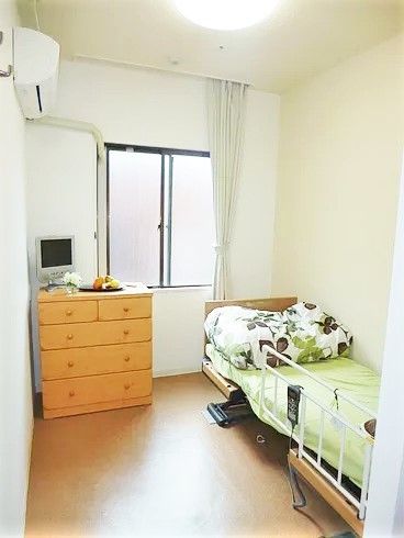 大きな白いカーテンが窓につけられ、たんすやテレビ、エアコン、ベッドなどの家具家電が設置されている。