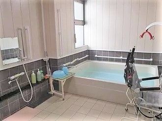 大きな四角い浴槽の周りには手すりが設置され、シャワーもある。リフト付きの浴室。