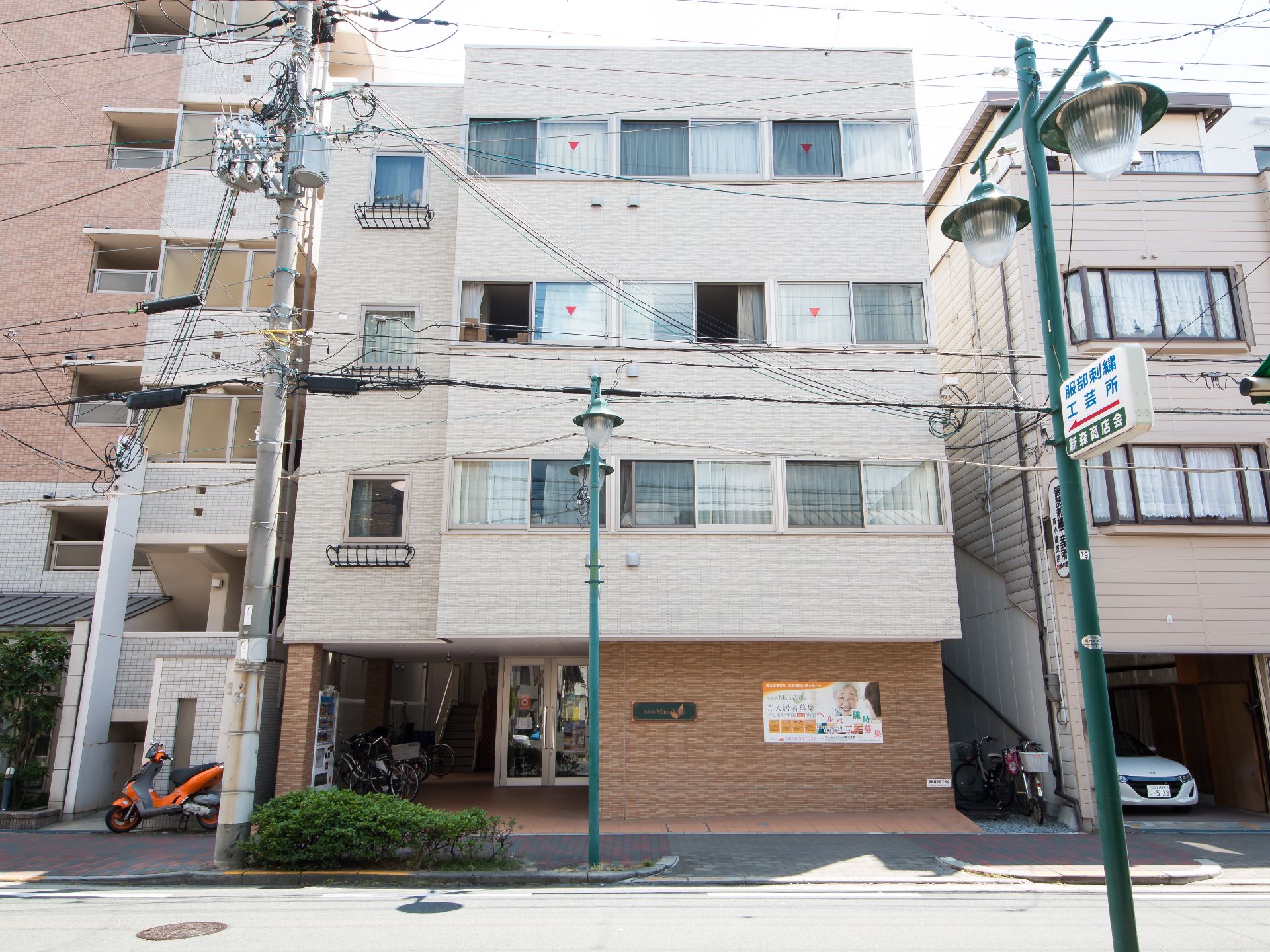 白を基調とした5階建ての建物の周りには自然が多く、玄関先には屋根が付いている。