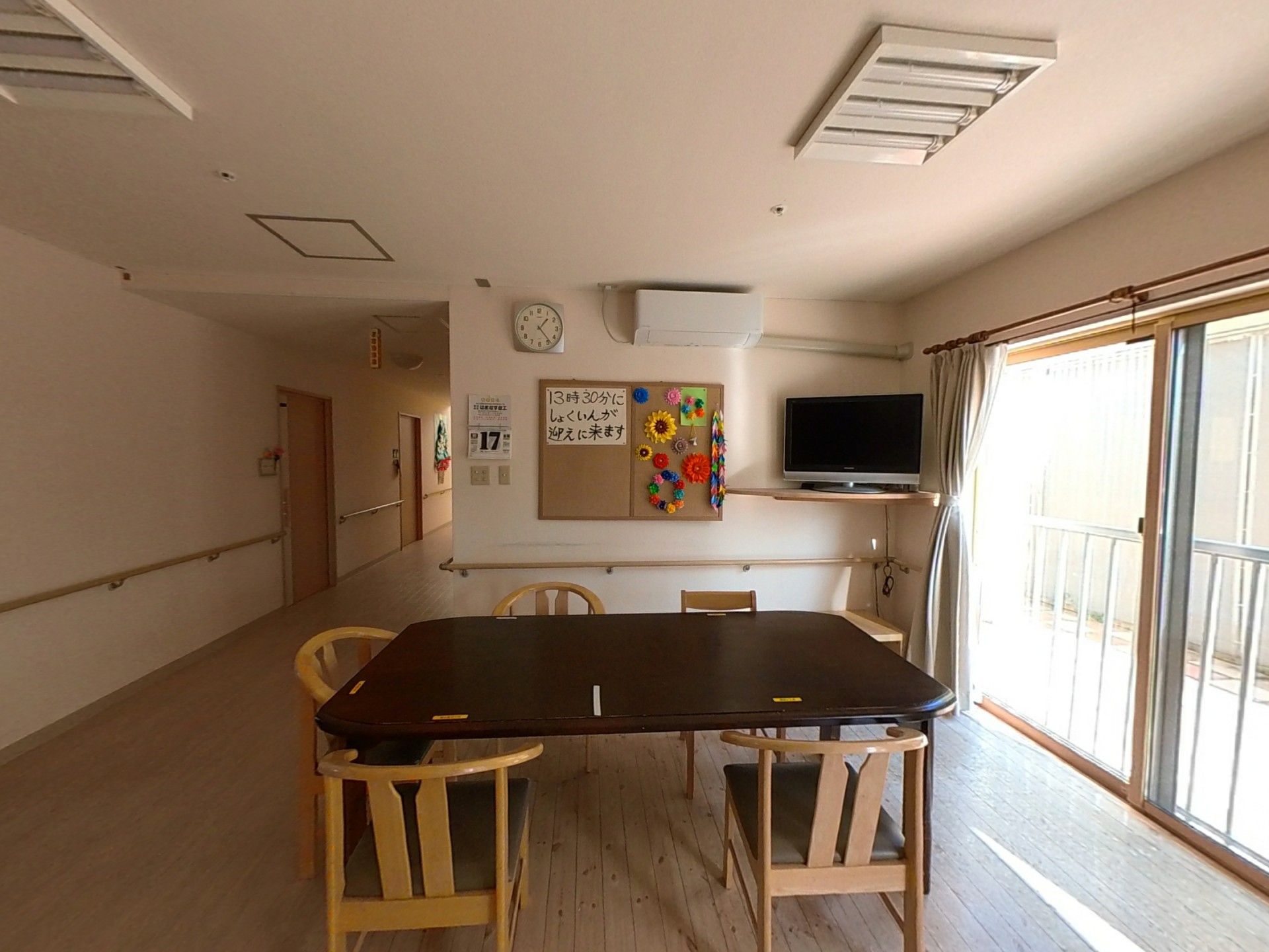 白衣を着た女性スタッフと高齢女性たちがベージュのソファを囲んで楽しそうに話している。