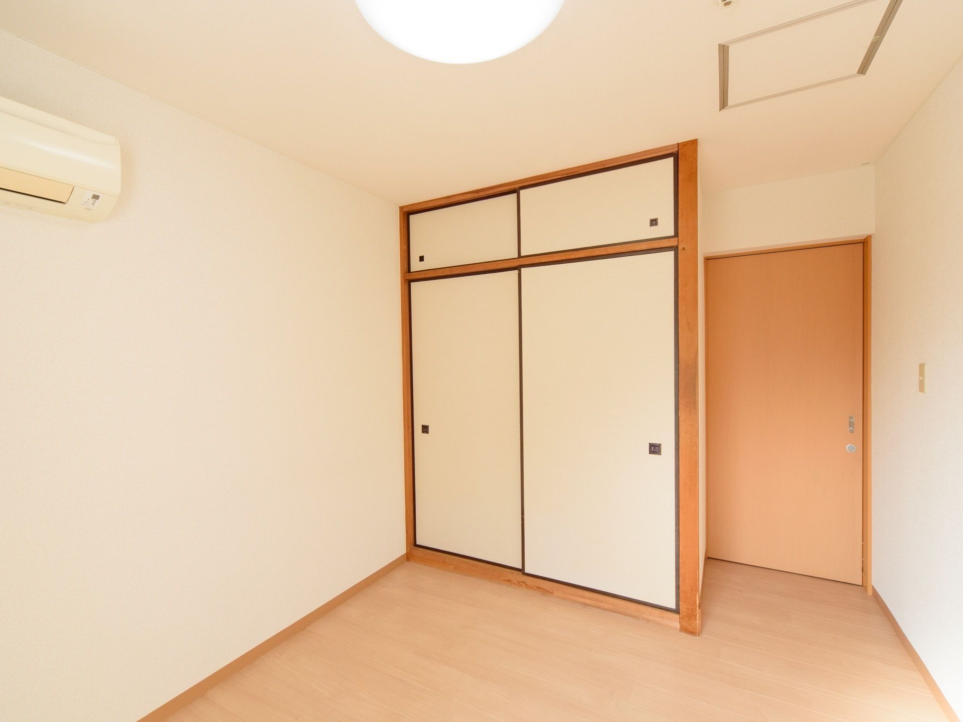 ドアの左側に、押入れが取り付けられている。床は、フローリングで明るい茶色である。居室の左側に、エアコンがある。