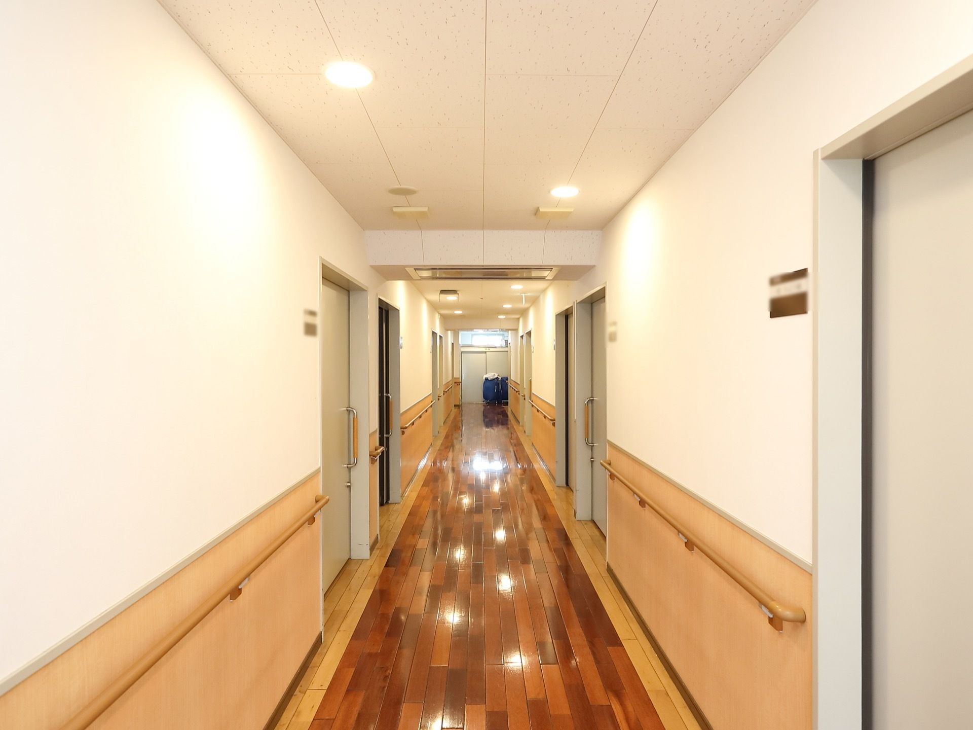 居室前の廊下である。あたたかみのある木目調で統一され、清掃が行き届いている。両サイドの壁には、手すりが設置されている。