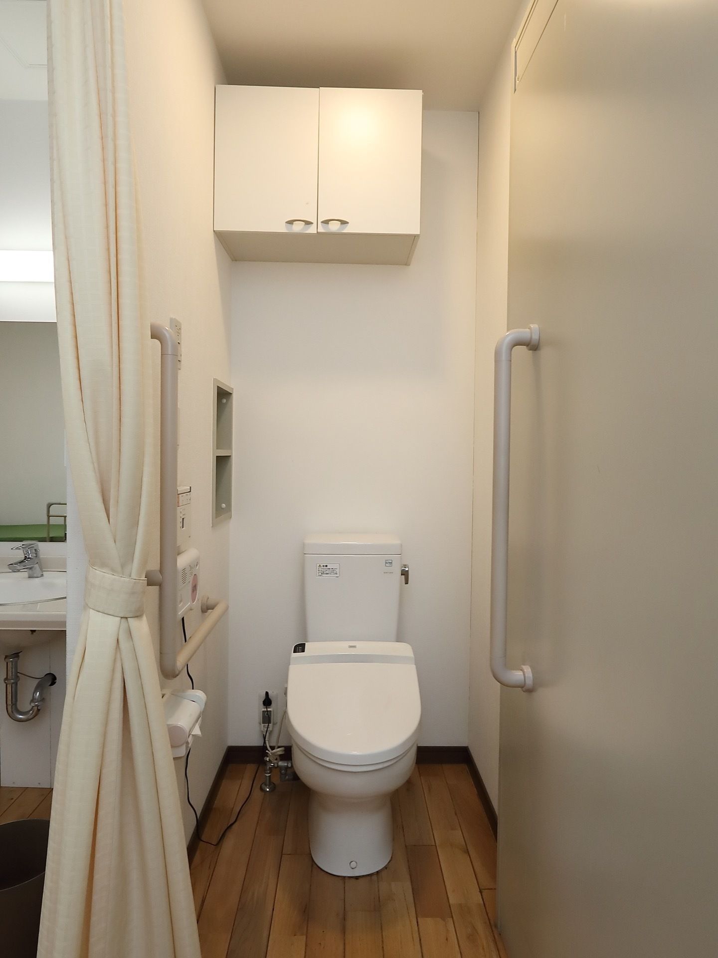 居室のトイレに完備されている温水洗浄便座器である。壁にはL字型手すりが設置され、カーテンで仕切りができるので、利用しやすい。