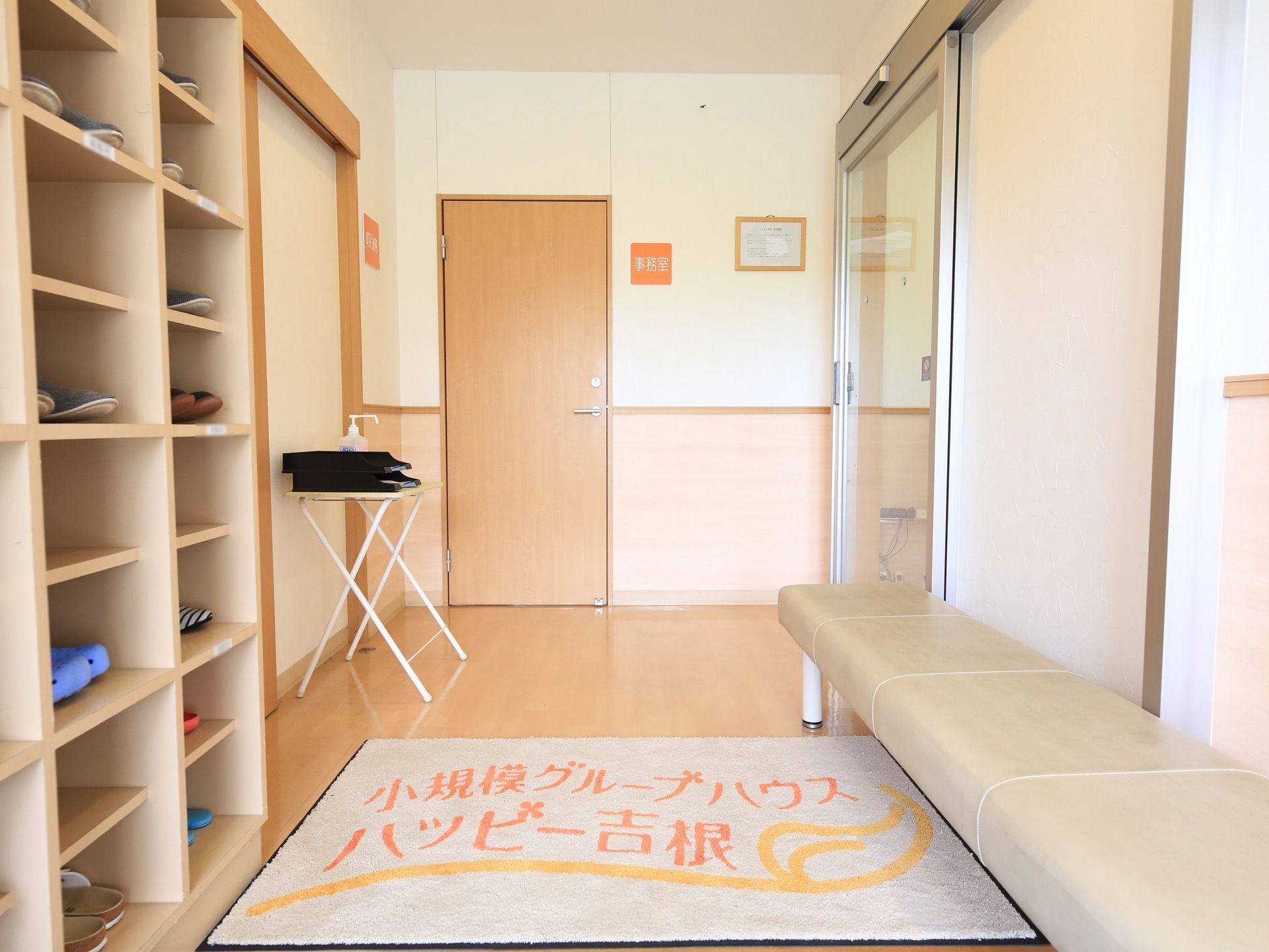 玄関にはベージュ色のベンチが置かれており、靴を脱いだり履いたりする際に座ることができる。消毒スプレーがある。