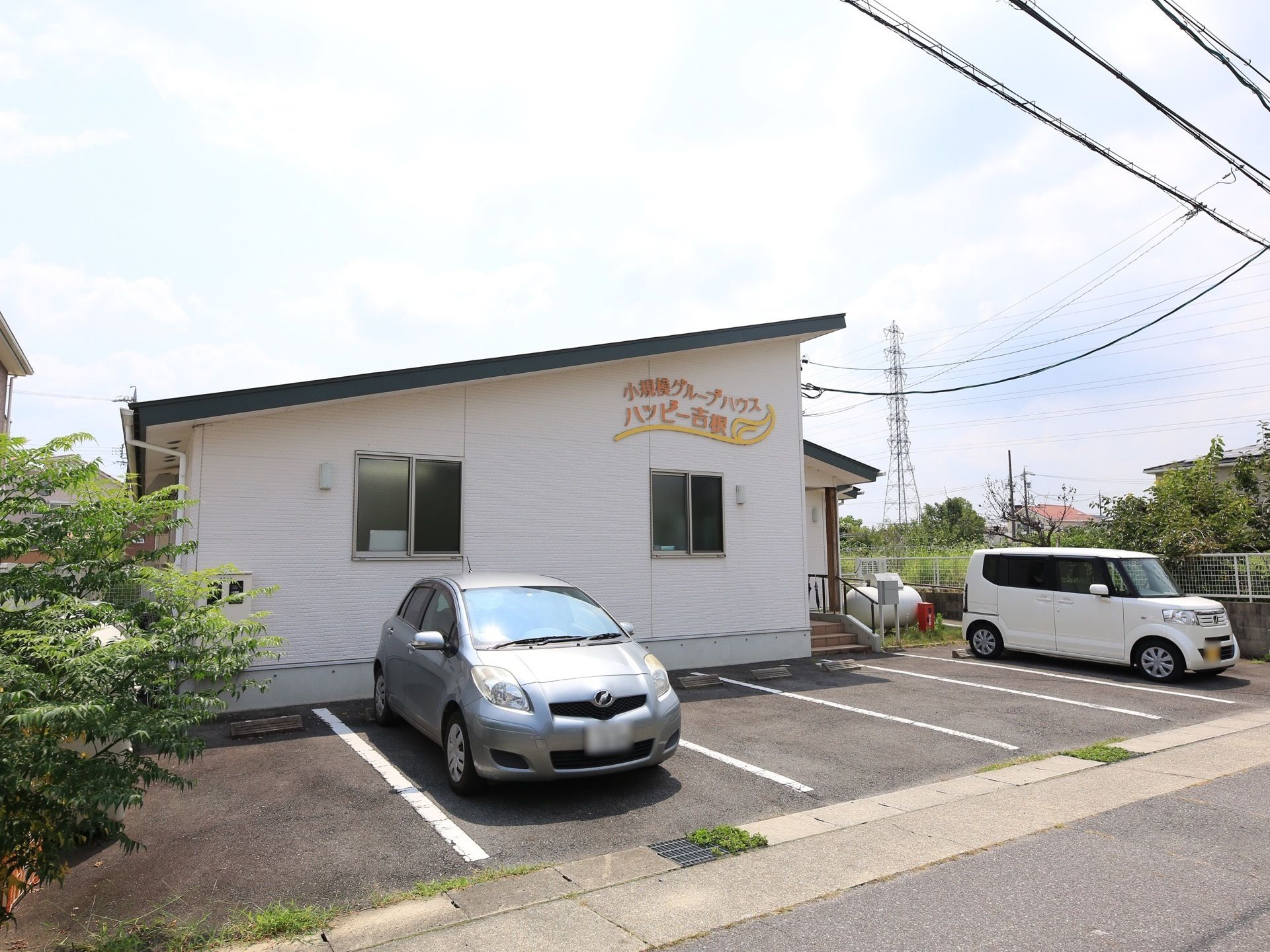 施設の外壁はクリーム色、オレンジ色で施設名が書かれており明るい雰囲気。建物の前には駐車場がある。