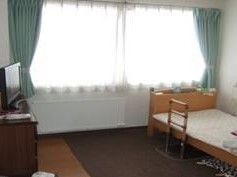 白いゆったりとした服を着た高齢女性がブルーのユニフォームを着た男性スタッフと一緒に笑顔で体操をしている様子。
