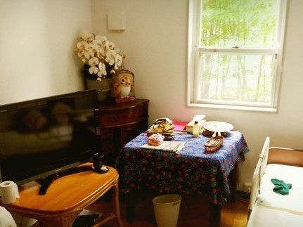 日用品やベッド、いすなどが並べられている居室の写真。窓の向こうに景色が見えている様子