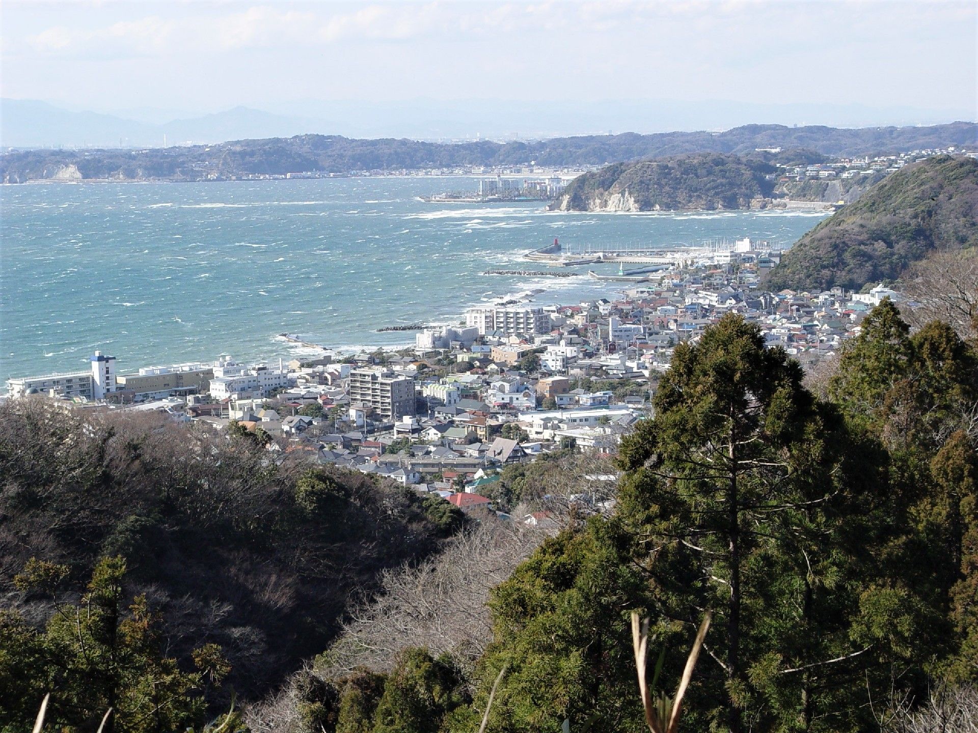 山の上から海岸沿いにある街を見下ろした様子。白波がきれいな青い海が広がっている。