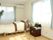 レースカーテンとカーテンが付いた大きな窓が２つあるフローリングの部屋には寝具が付いた介護ベッドや小さな収納棚がある。