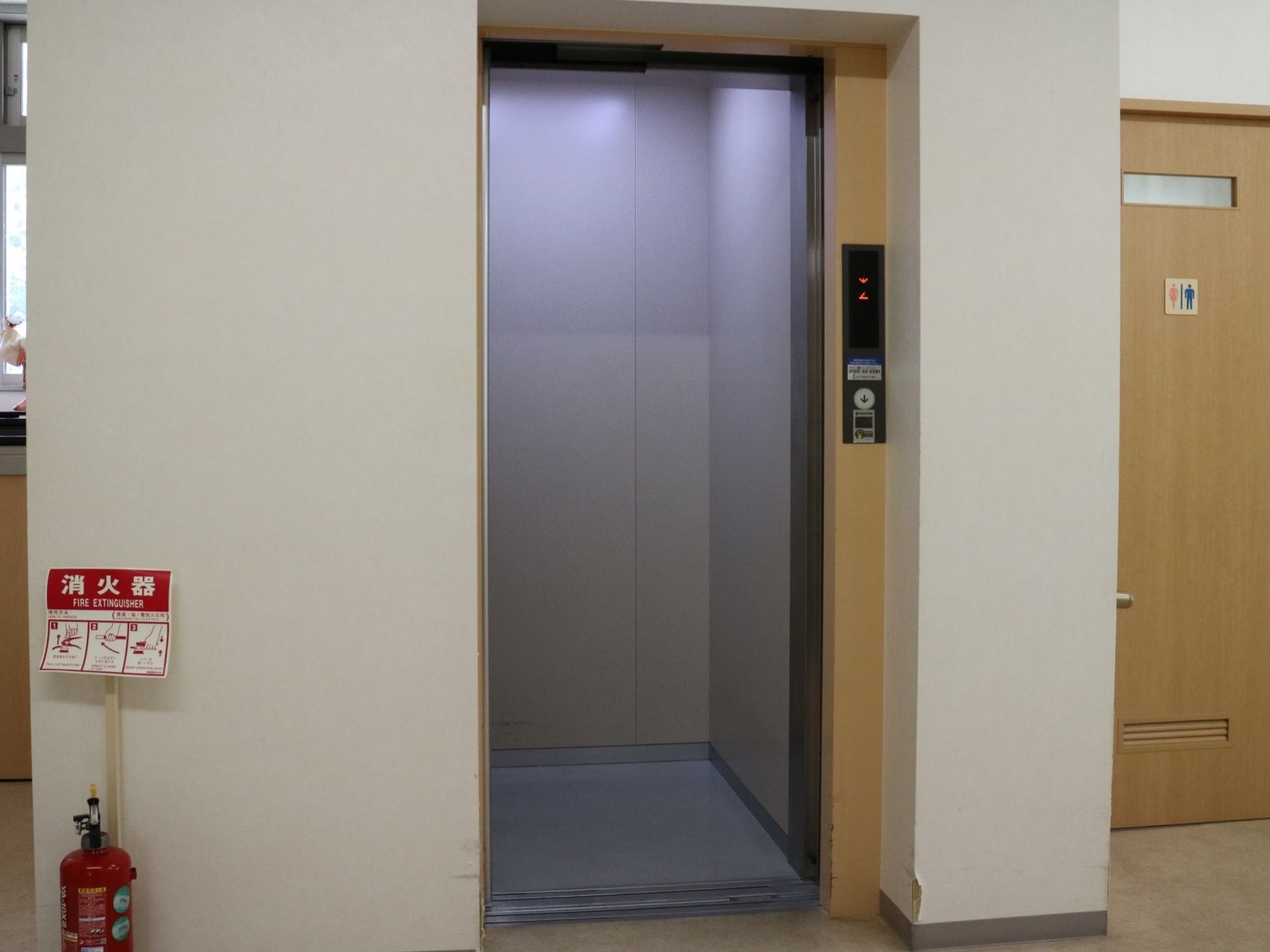 エレベーターがある。エレベーター乗降口の左側に消火器が置かれている。右側にはトイレの入口扉がある。