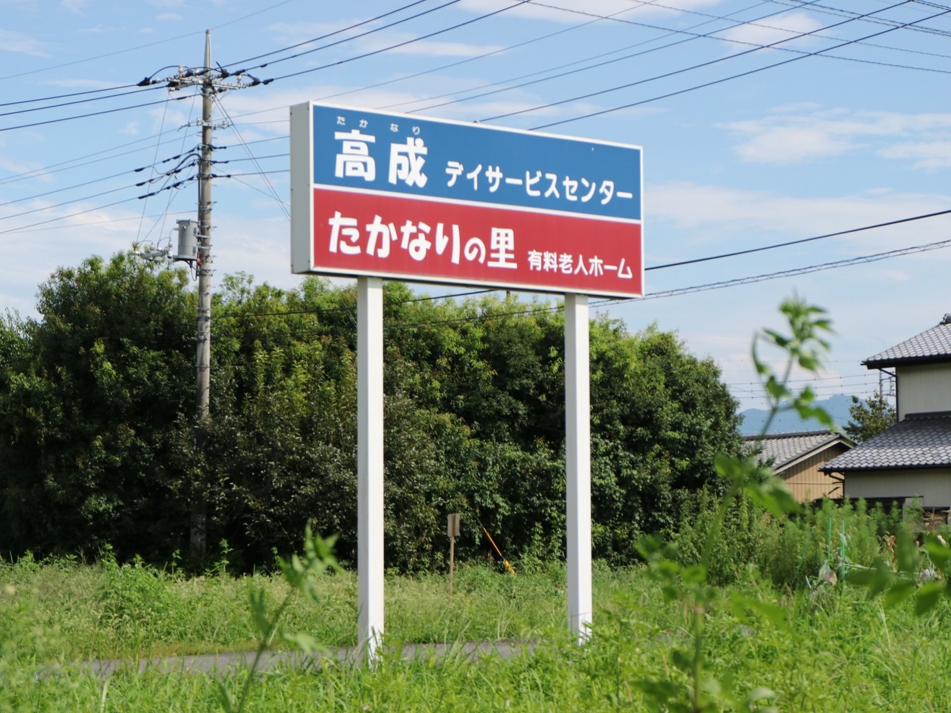 道路沿いの高い位置に、施設の看板がある。２種類の施設名称とそれぞれの提供サービスが色分けして表示されている。