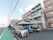 ５階建ての建物が３棟つながっている施設である。敷地の目の前が道路で、歩道部分が緑色の舗装になっている。