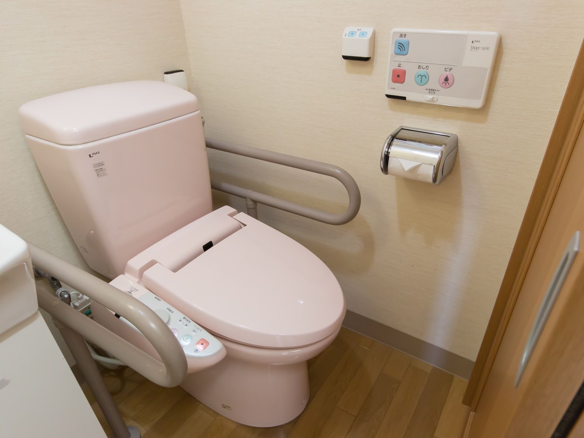 トイレにピンク色の便座が設置されている。便座の両側に手すりが付けられているトイレットペーパーの先が折りたたまれている。