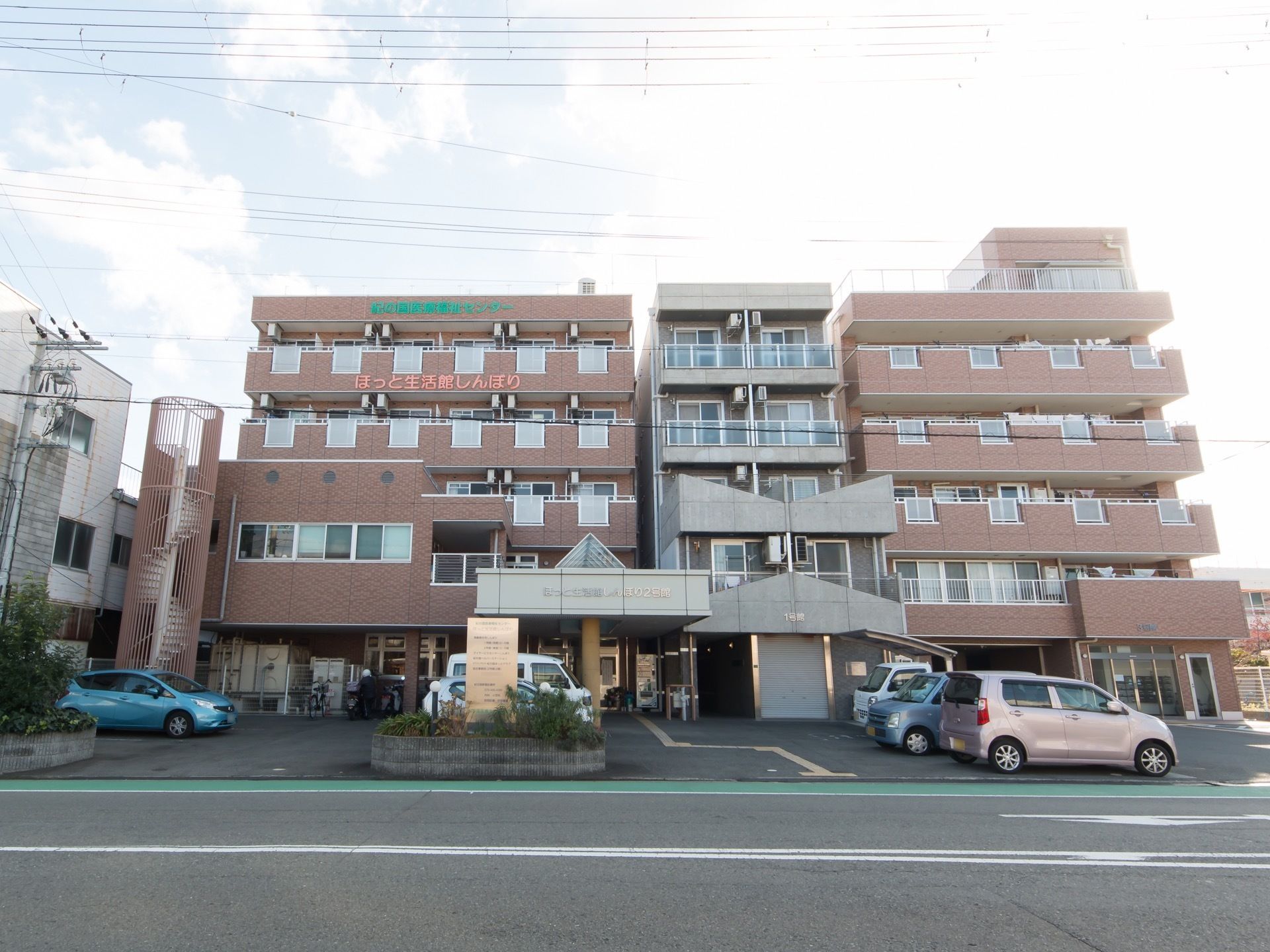 道路から玄関まで黄色の点字ブロックが敷かれている。柵のついた回り階段が建物の一番左側に設置されている。
