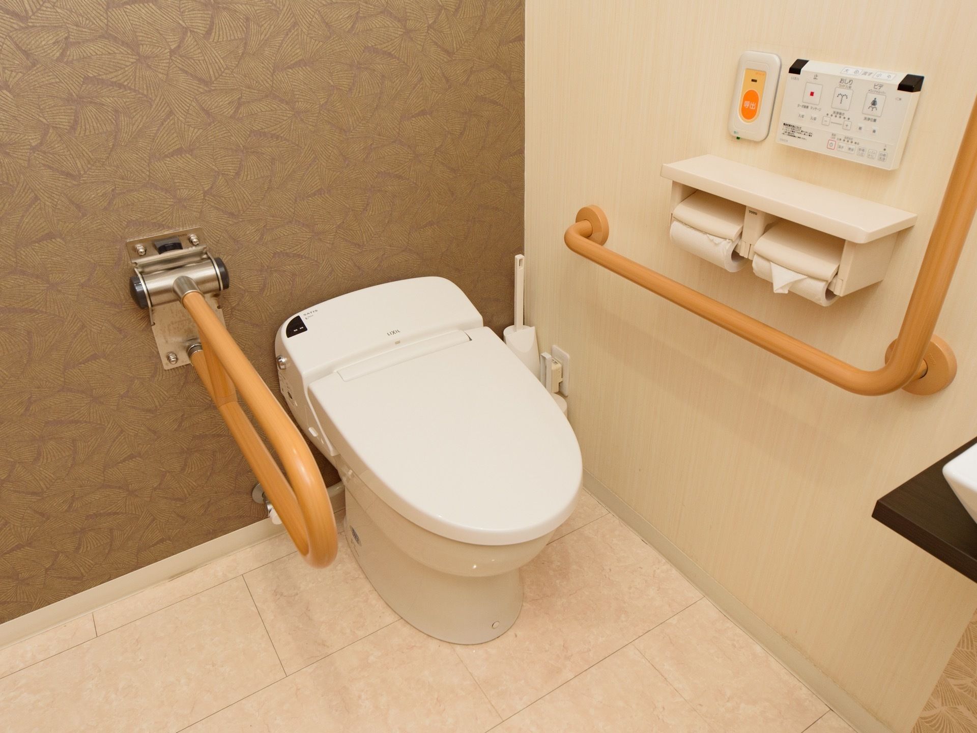 温水洗浄機能付きのトイレで、便器の両サイドには手すりが設置されている。個室内に洗面台が備え付けられている。