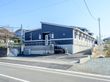 濃紺の壁に白い線が描かれた爽やかな印象の外観である。道路から正面には勝手口があり、正面玄関は奥まった場所にある。