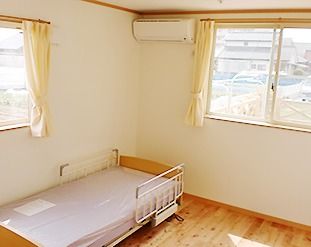カーテンが付いた大きな窓がある居室はフローリングで、ベッドが置かれている。