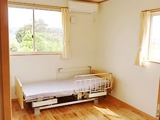 介護ベッドが置かれた居室には大きな窓が二つ付き、カーテンが付けられている。