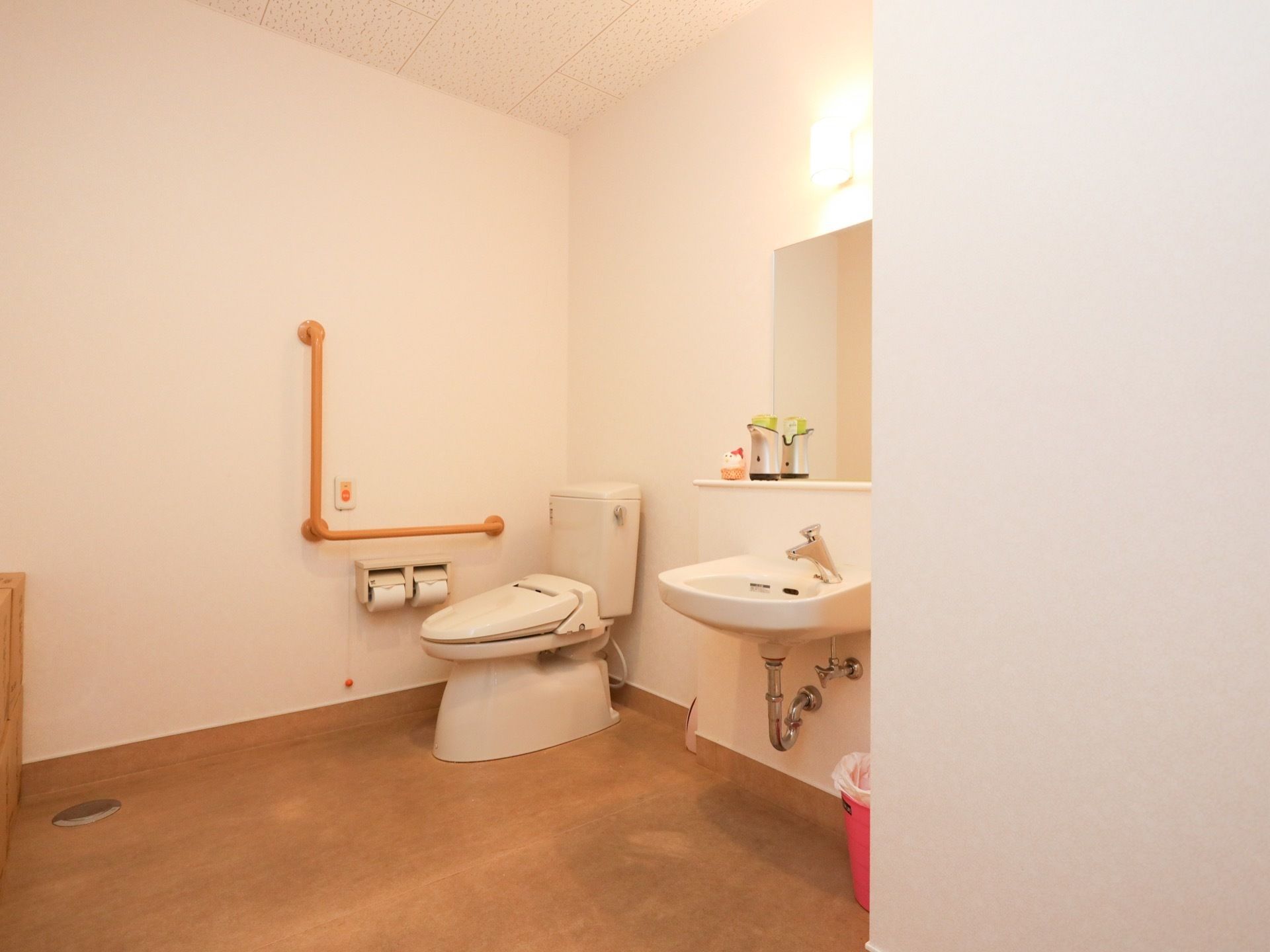 トイレの個室は広い。壁にはL字型の手すりが設置されており、その近くに緊急呼び出し用のボタンが取り付けられている。
