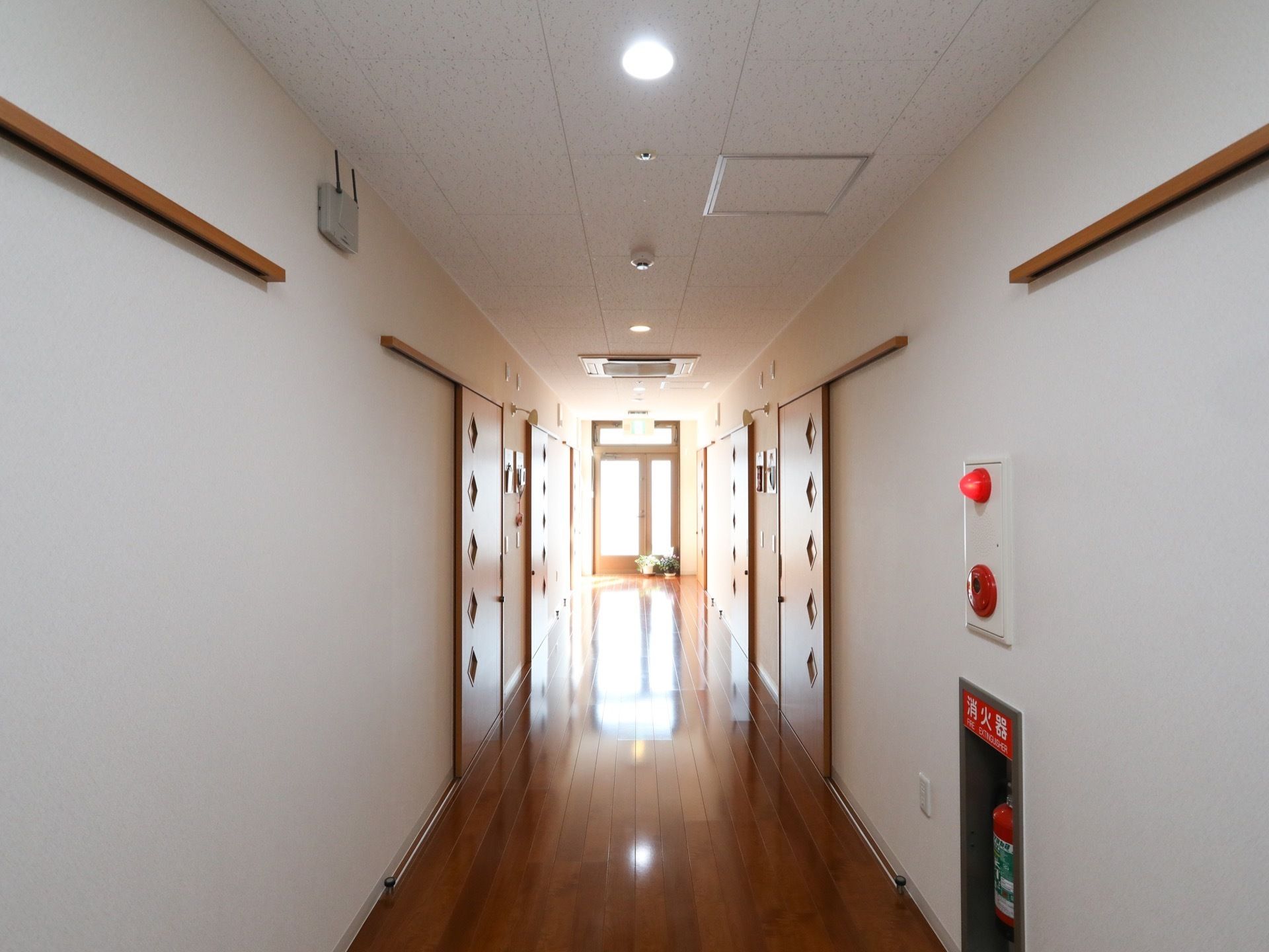 通路の壁には消火器などの消防設備が取り付けられている。通路の両側に並ぶ居室のドアはスライド式で、ダイヤ型の模様があしらわれている。