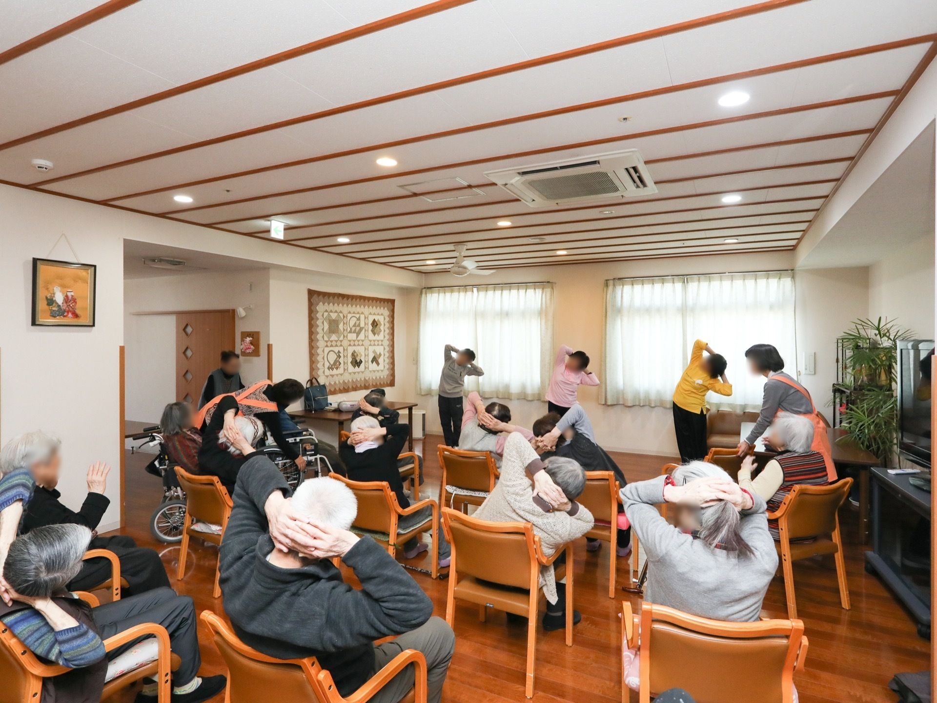 共有スペースで、入居者様が集まり、椅子に座って体操を楽しんでいる。車椅子をご利用の方もご参加いただける。