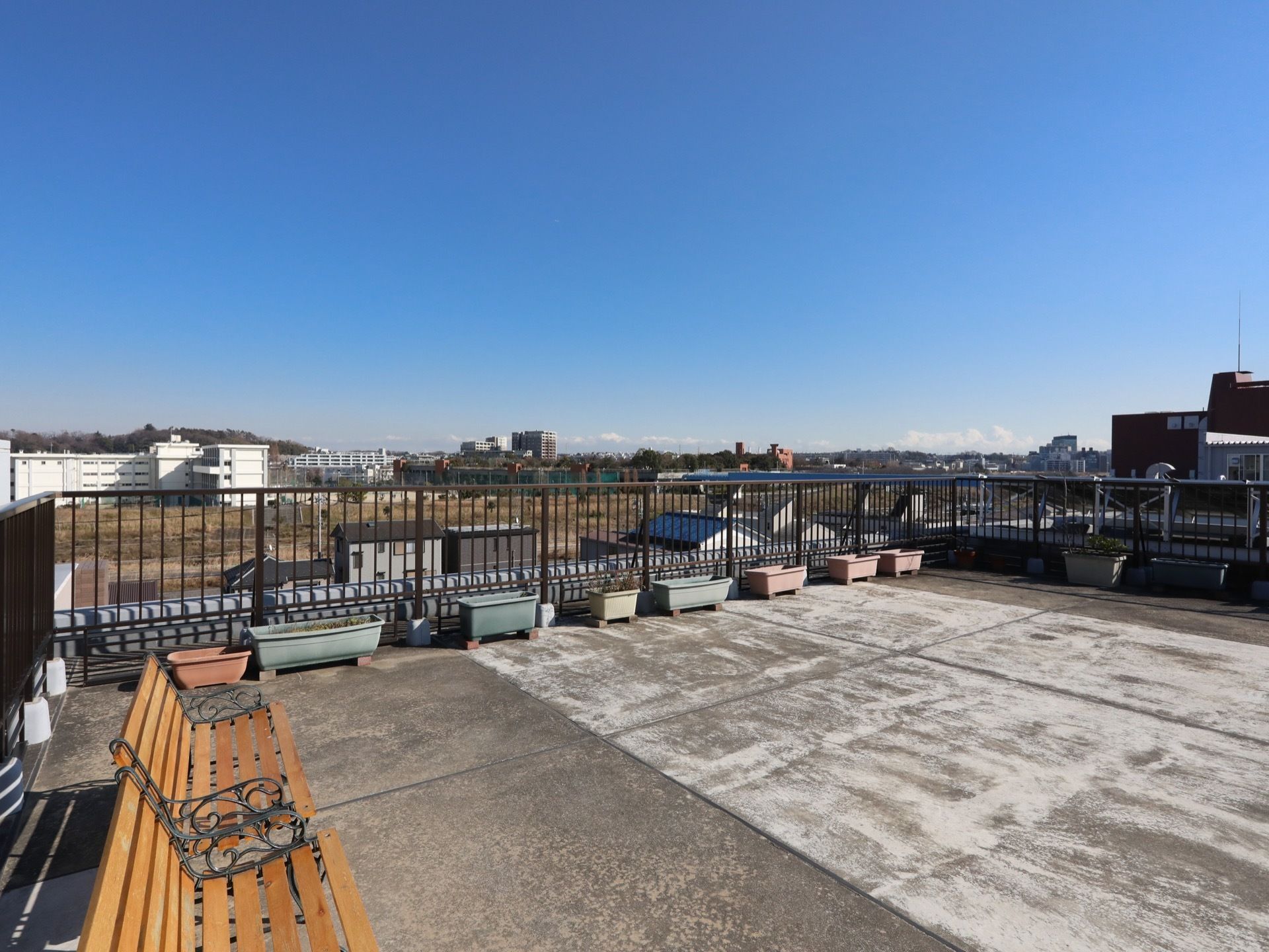 入居者様が安全に屋上に出られるよう、屋上には柵を取り付けている。柵の周囲にはプランターが置かれている。木製のベンチが並べられている。