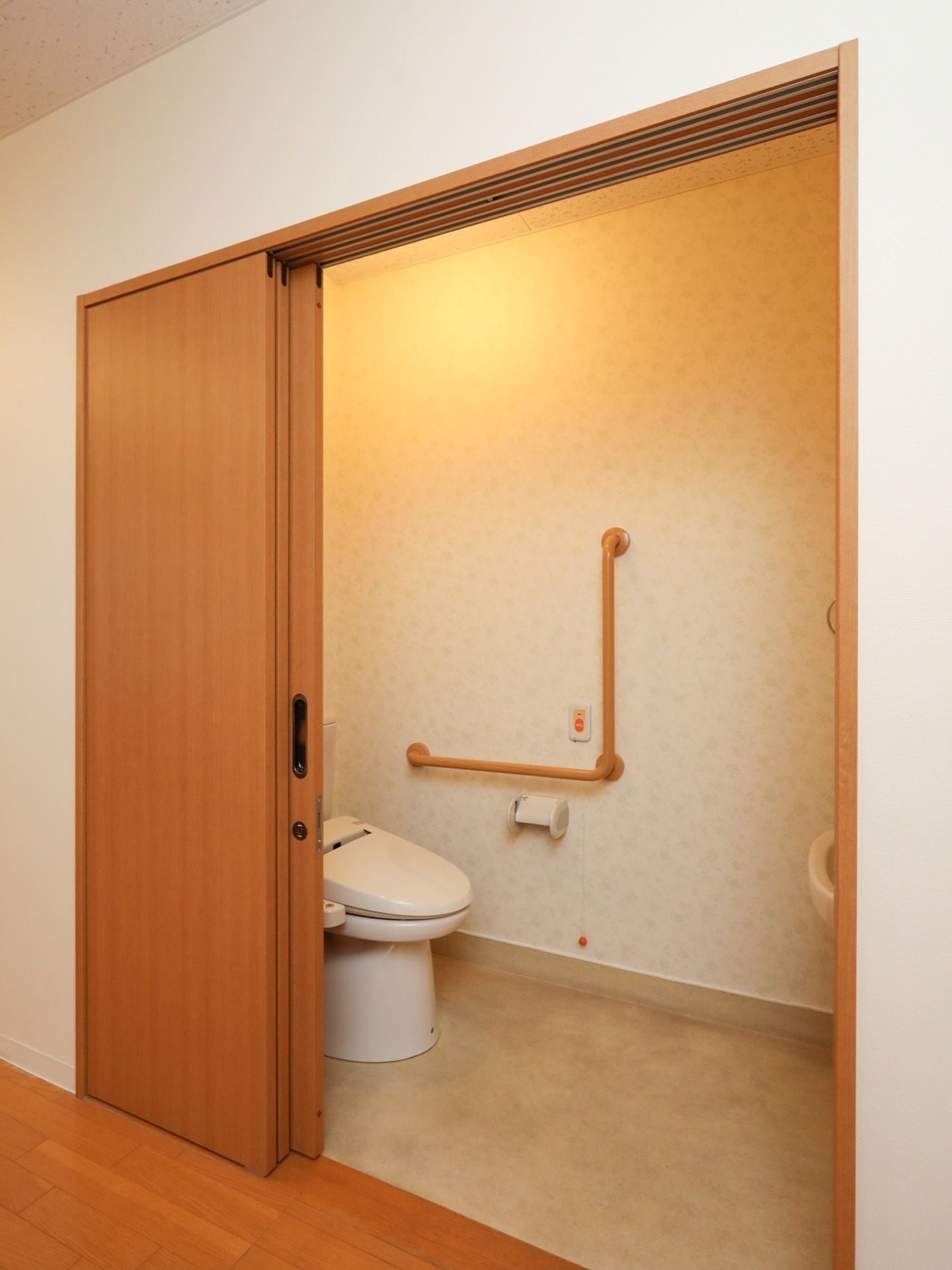 居室のトイレの入り口はスライド式ドアである。便器の前には広いスペースがある。壁には手すりが取り付けられている。