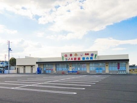 たくさんの野菜が描かれている外壁の平屋建てのスーパーマーケット。広い駐車場が付いている。