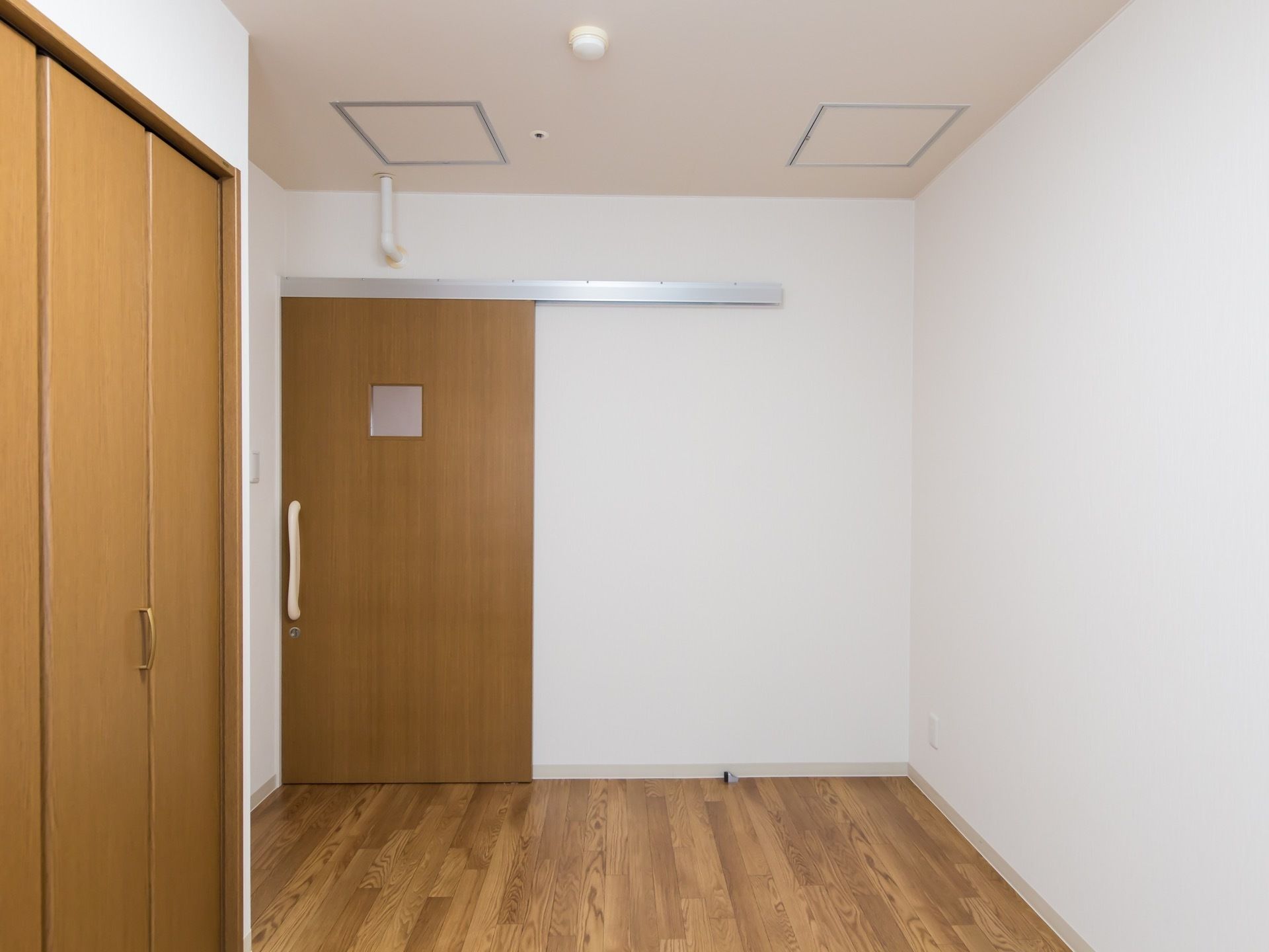 木目調のフローリングと白い壁の居室がある。引き戸のドアが付いており、同じ色調の扉のクローゼットがある。