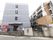 坂道の道路に面した場所に４階建ての建物が建っている。青いタイルで覆われ、コンクリートブロックの塀とフェンスがあり、鉄製の門扉が付いている。