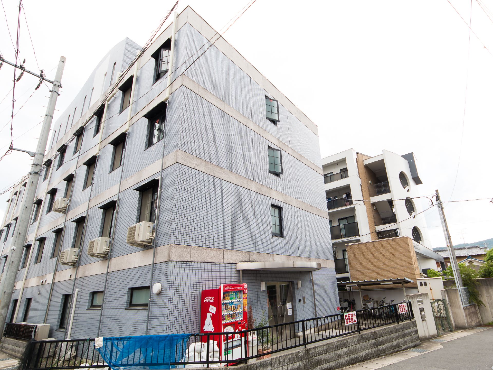 ４階建ての鉄骨製の建物。周辺には緑が多く、窓も多く設置されている。