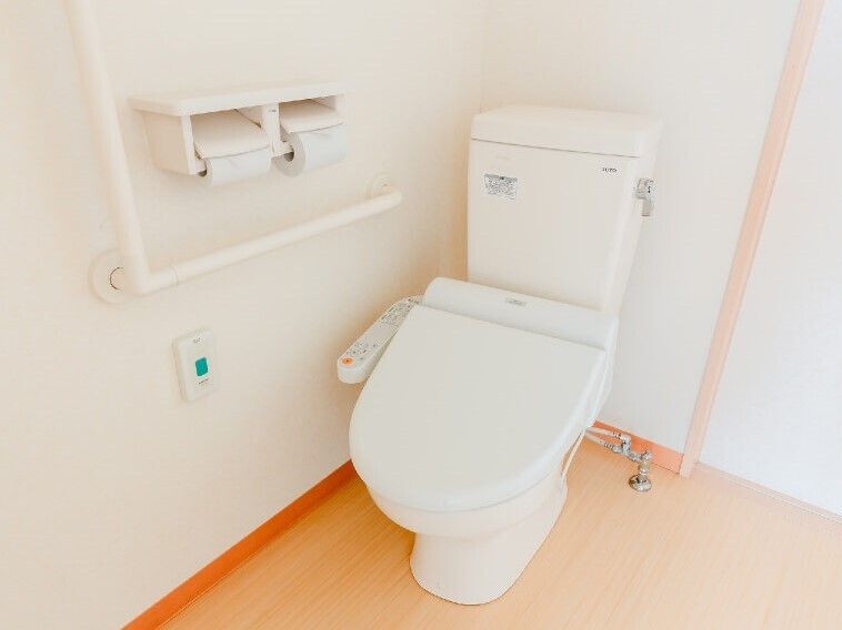 エル字型の手すりや呼び出しボタンが洋式トイレの横につき、トイレットペーパーホルダーも設置されている。