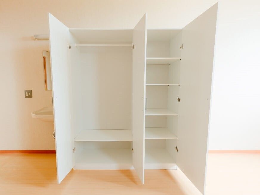 洗面所の横にある白い大きな収納家具。扉を開けると棚やポールが設置され、整理しやすくなっている。