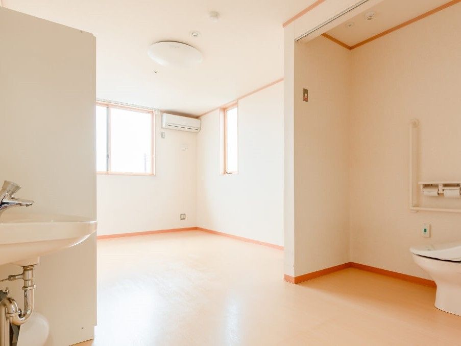 フローリングの居室。家具はなく、オープンな造りのトイレと車いす対応の洗面所、エアコンが付いている。