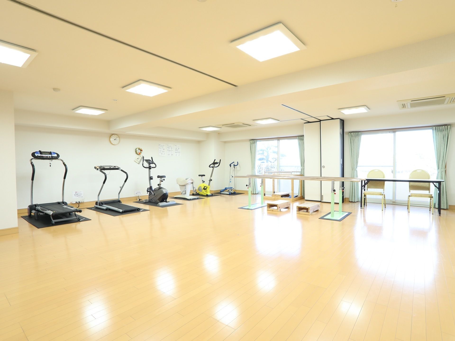 広々としたフロアの、機能訓練室がある。段差のない床で、大きなガラス窓にカーテンが取り付けられている。