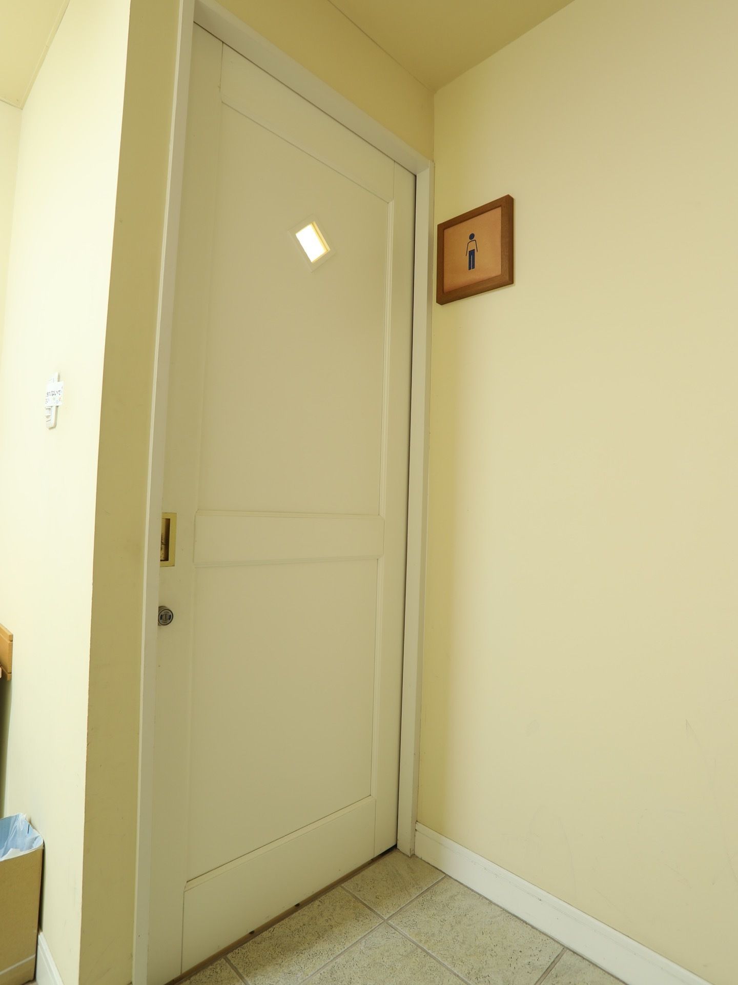 トイレ入口の壁は清潔感のある白色で、男性用のプレートが取り付けられている。扉には、小窓が用意されている。