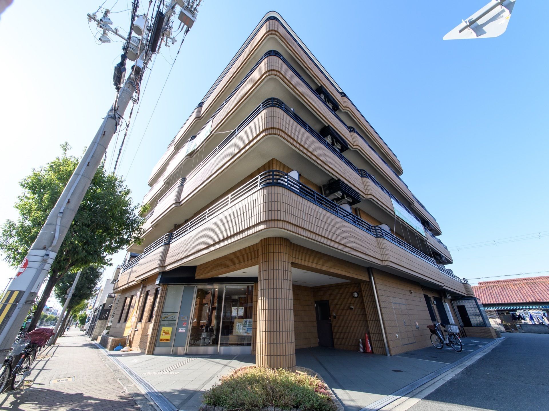 茶色い外装の建物である。施設名が表示されている。エントランス付近はひさしになっている。駐輪スペースがある。