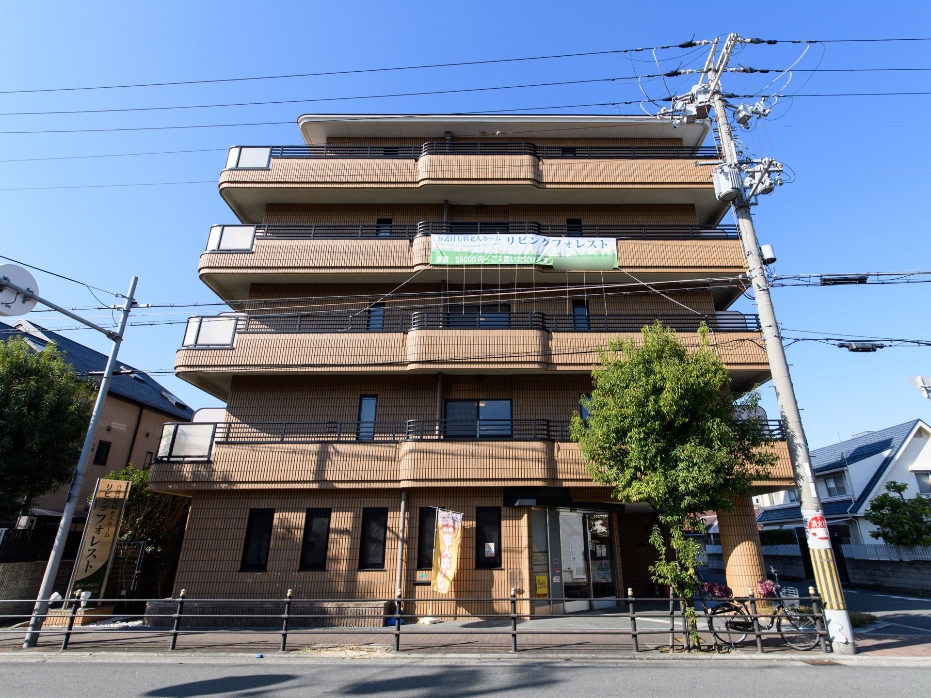 ５階建ての建物には、施設名が表示された横断幕がかけられている。２階以上の居室にはベランダが付いている。