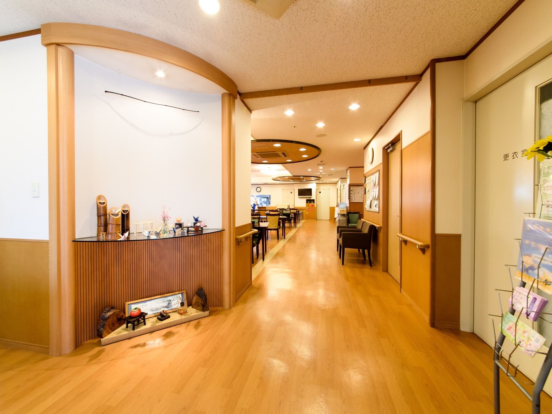 和風の小物がたくさん飾られている。更衣室の扉がある。奥のフロアには複数のイスとテーブルがある。手すりが設置されている。