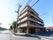 5階建ての施設である。ベランダが付いている。駐輪スペースに自転車が１台停まっている。道路に面している。